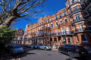A row of red brick townhouses with multiple stories, typical of a historic urban area. - Beautifully renovated 2-bedroom, 2-bathroom garden apartment in the heart of Kensington & Chelsea, featuring a spacious king en-suite, flexible bedding, bright living areas, and elegant finishes — perfect for families, friends, or business stays. (Greater London)