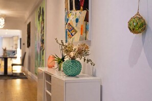 A hallway with a white console table holding a decorative vase with dried flowers and a textured green vase. - Beautifully renovated 2-bedroom, 2-bathroom garden apartment in the heart of Kensington & Chelsea, featuring a spacious king en-suite, flexible bedding, bright living areas, and elegant finishes — perfect for families, friends, or business stays. (Greater London)