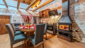 A cozy dining area with a stone wall, wooden beams, a built-in wood stove, and a kitchen with a stone facade. - Villa Niko Zadarvillas (Škabrnja)
