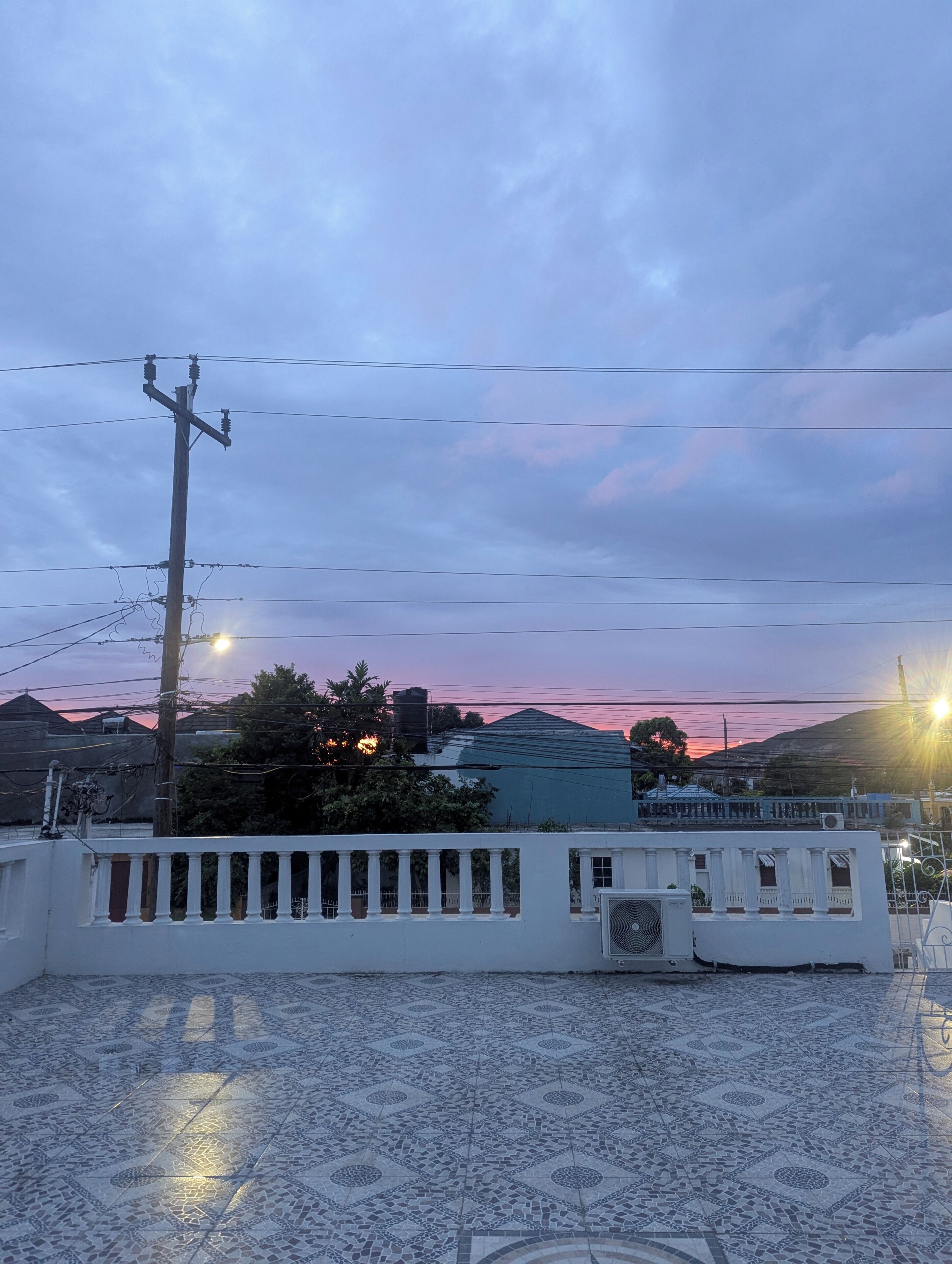 Una terraza en la azotea con baldosas estampadas, barandilla blanca y vistas al atardecer.