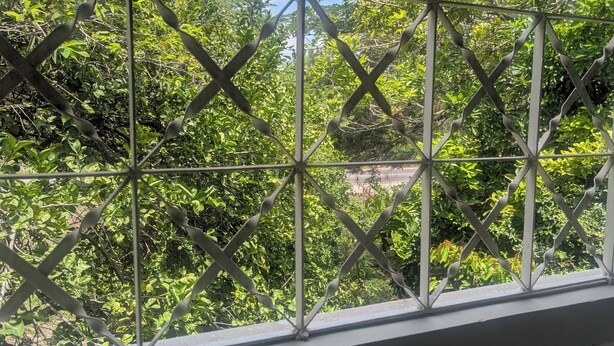 Vista a través de una ventana de celosía metálica con barandilla de balcón.