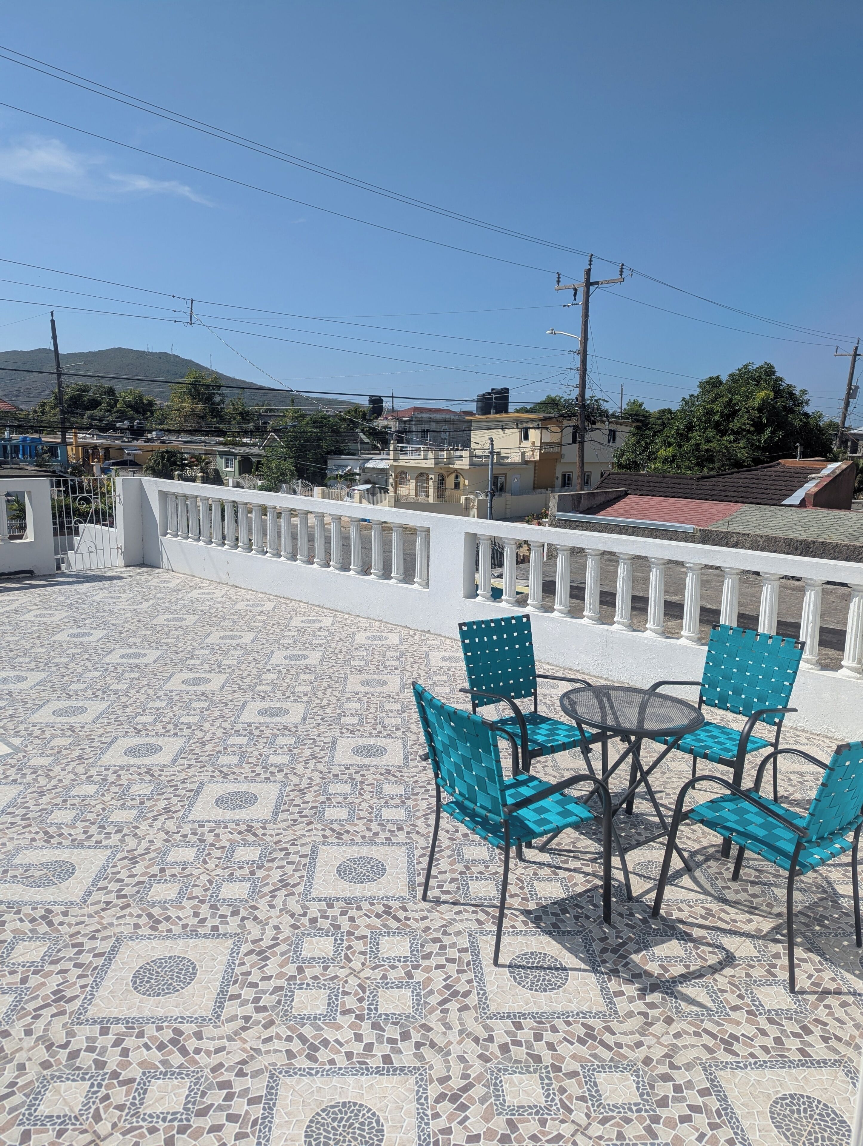 A terrace with mosaic flooring, a white railing, and blue chairs with a table.