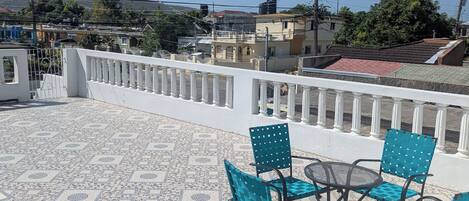 A terrace with mosaic flooring, a white railing, and blue chairs with a table.