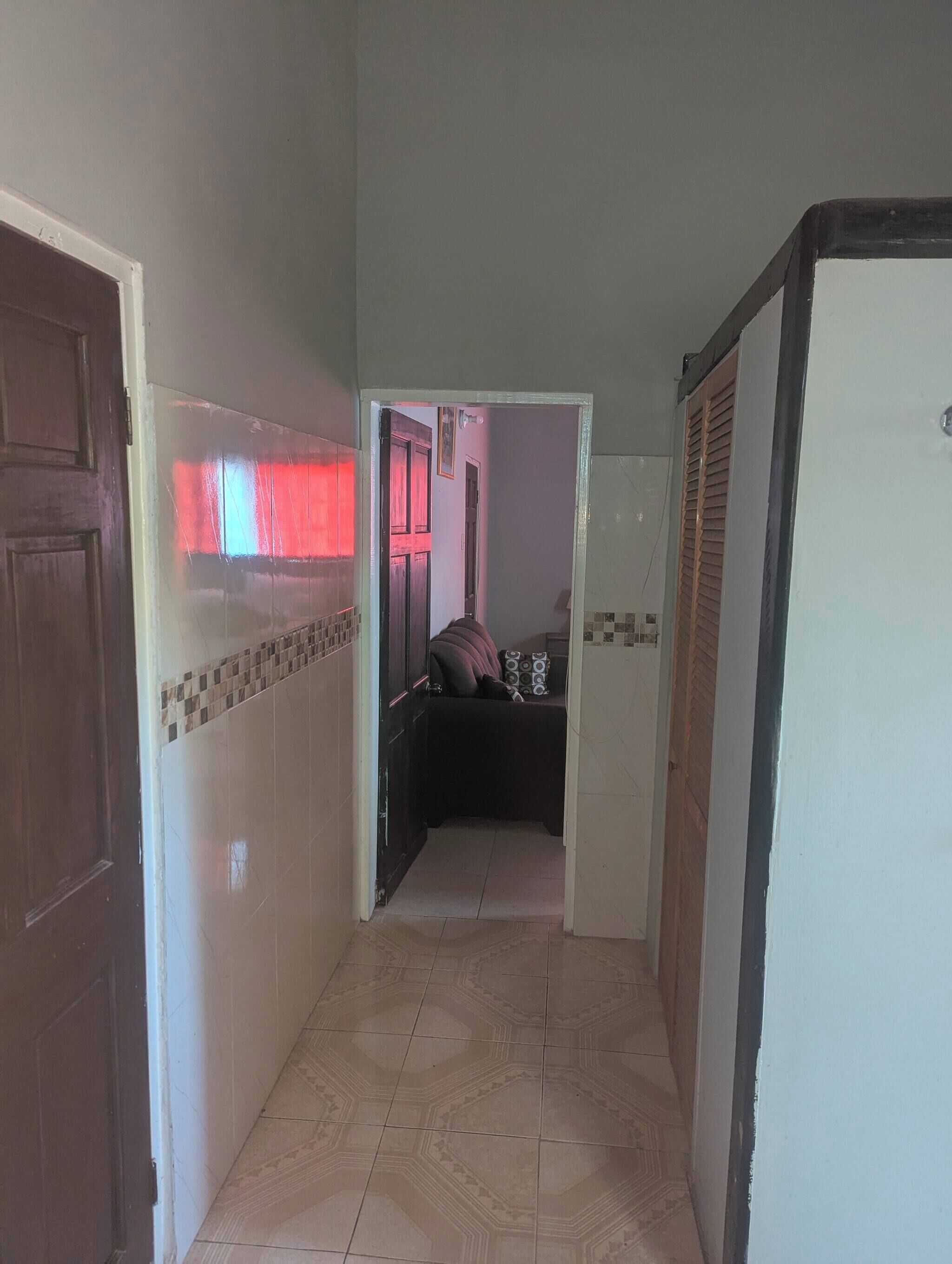 A hallway with a tiled floor, a wooden door on the left, and a white door on the right.