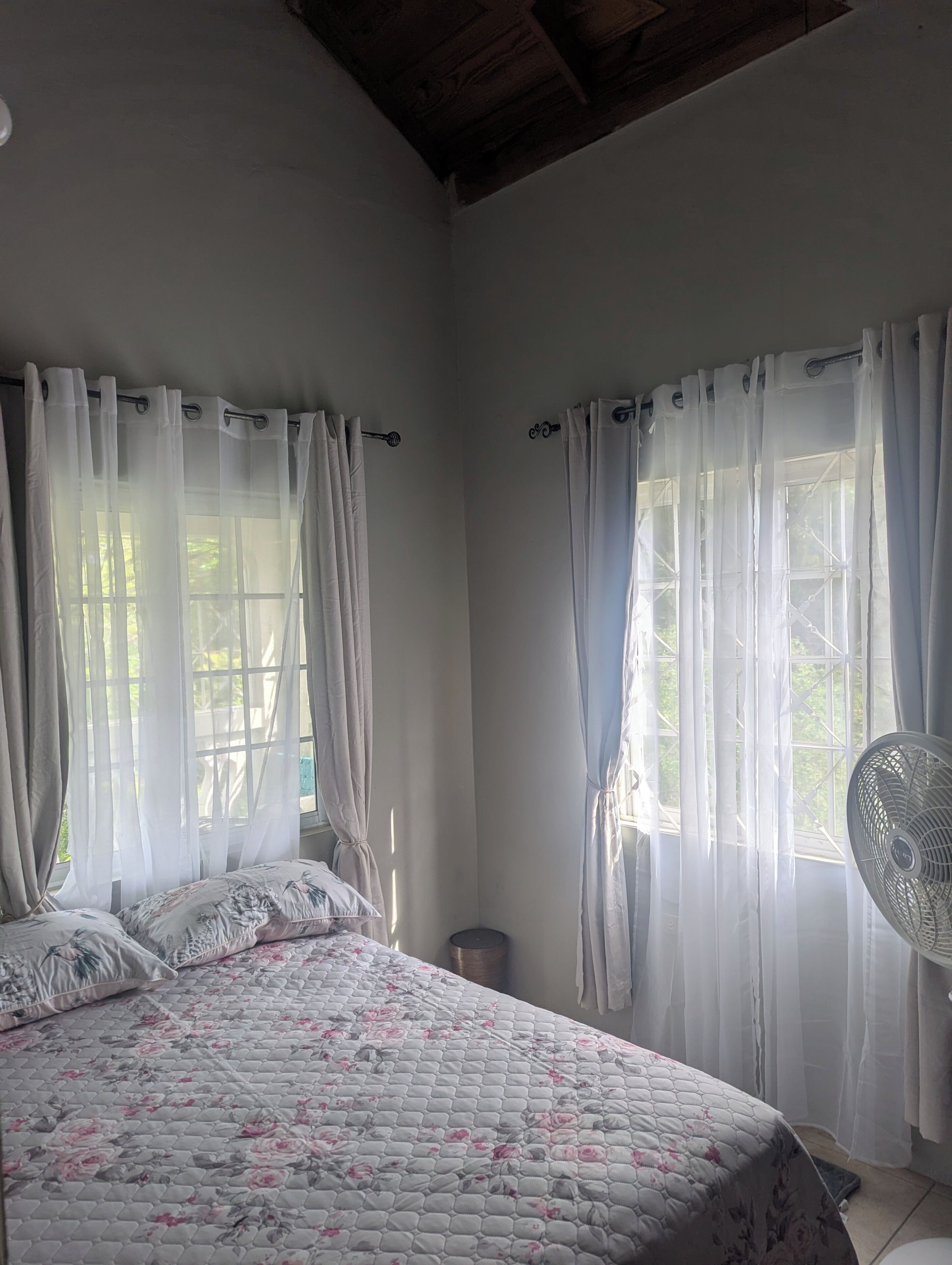 Une chambre à coucher avec un lit, des rideaux, un ventilateur et une fenêtre.