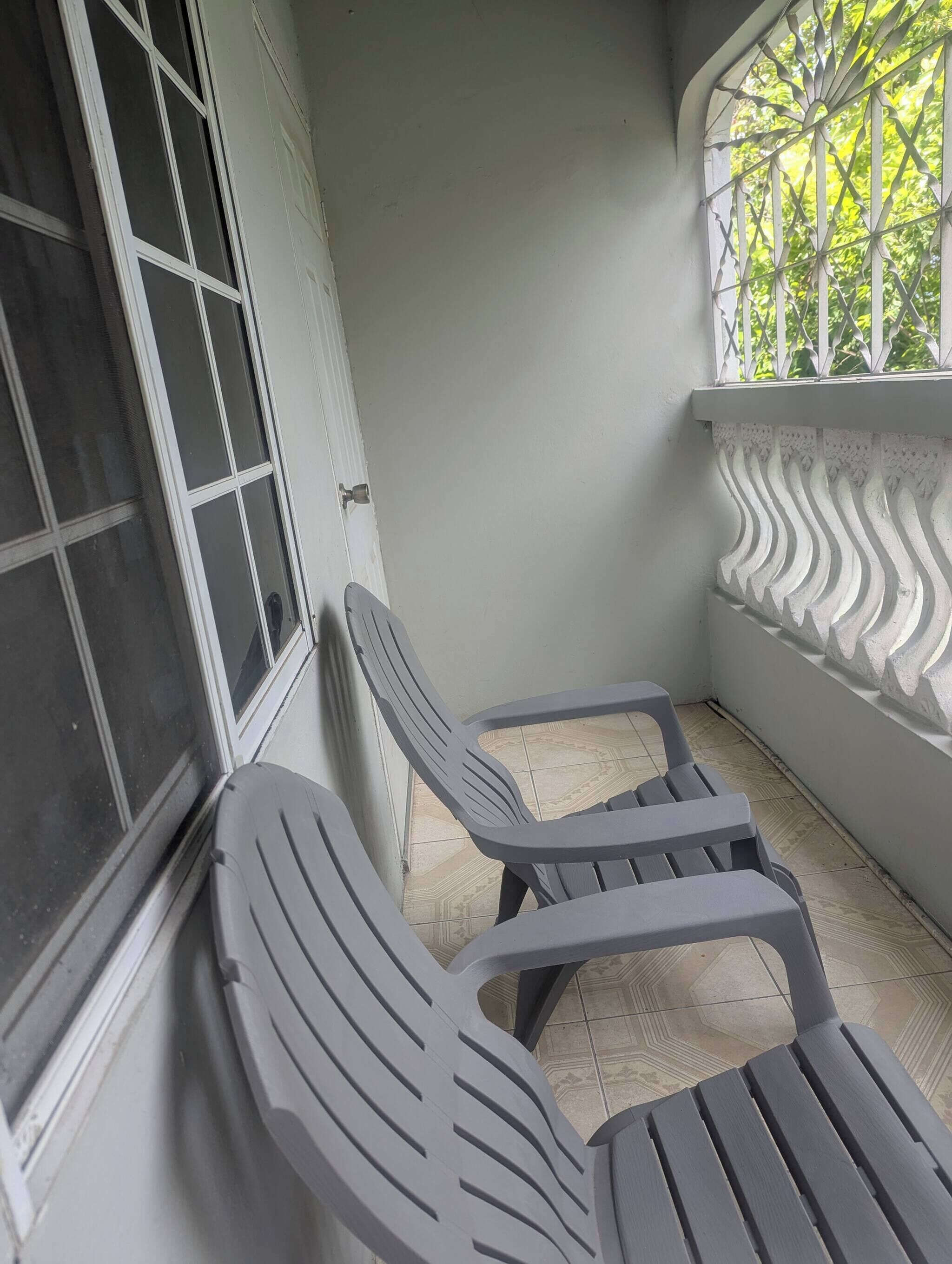 A balcony with two plastic chairs, a white door, and a window with metal bars.