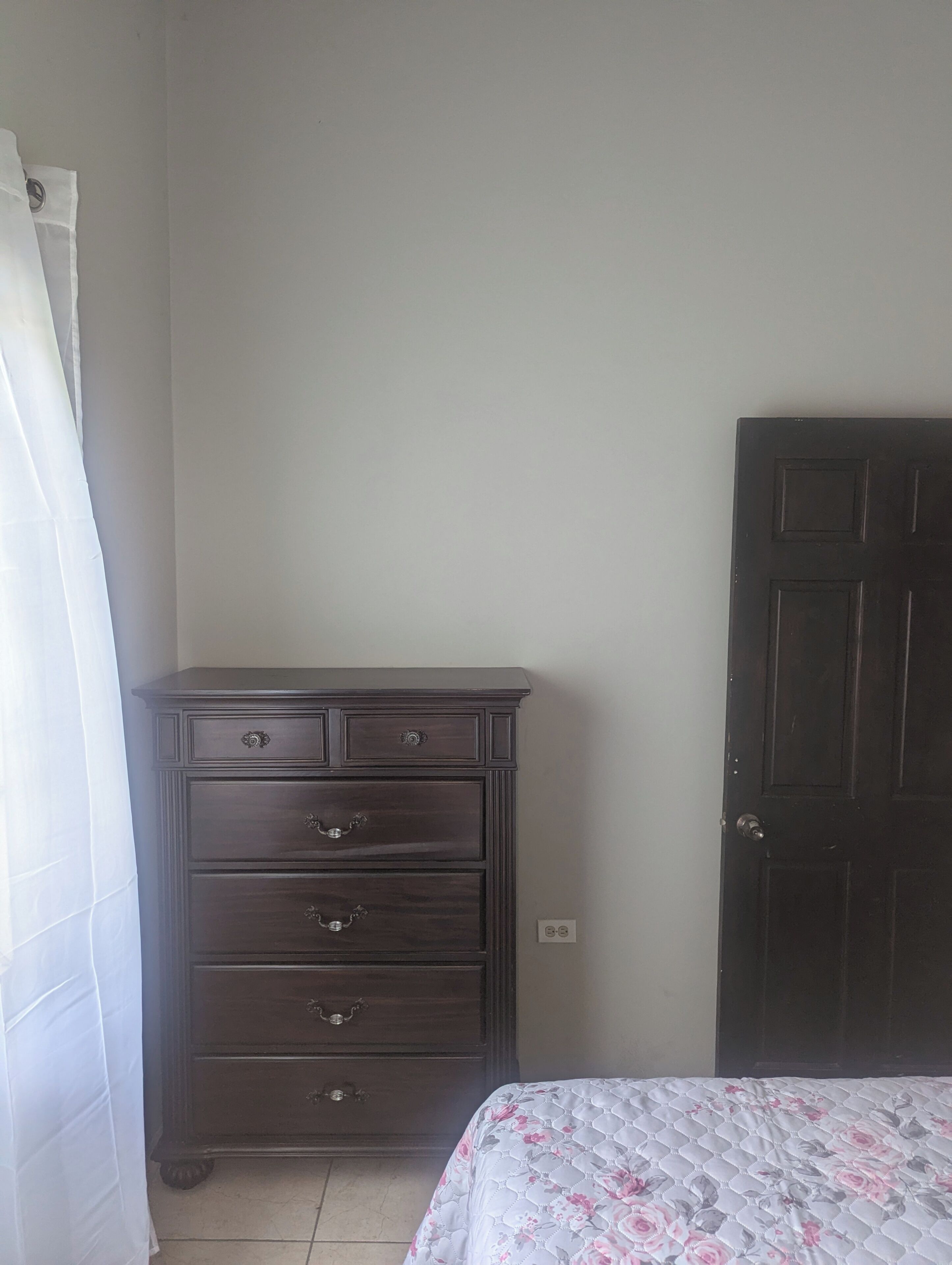 A bedroom with a dark wooden dresser, a door, and a bed with a floral bedspread.