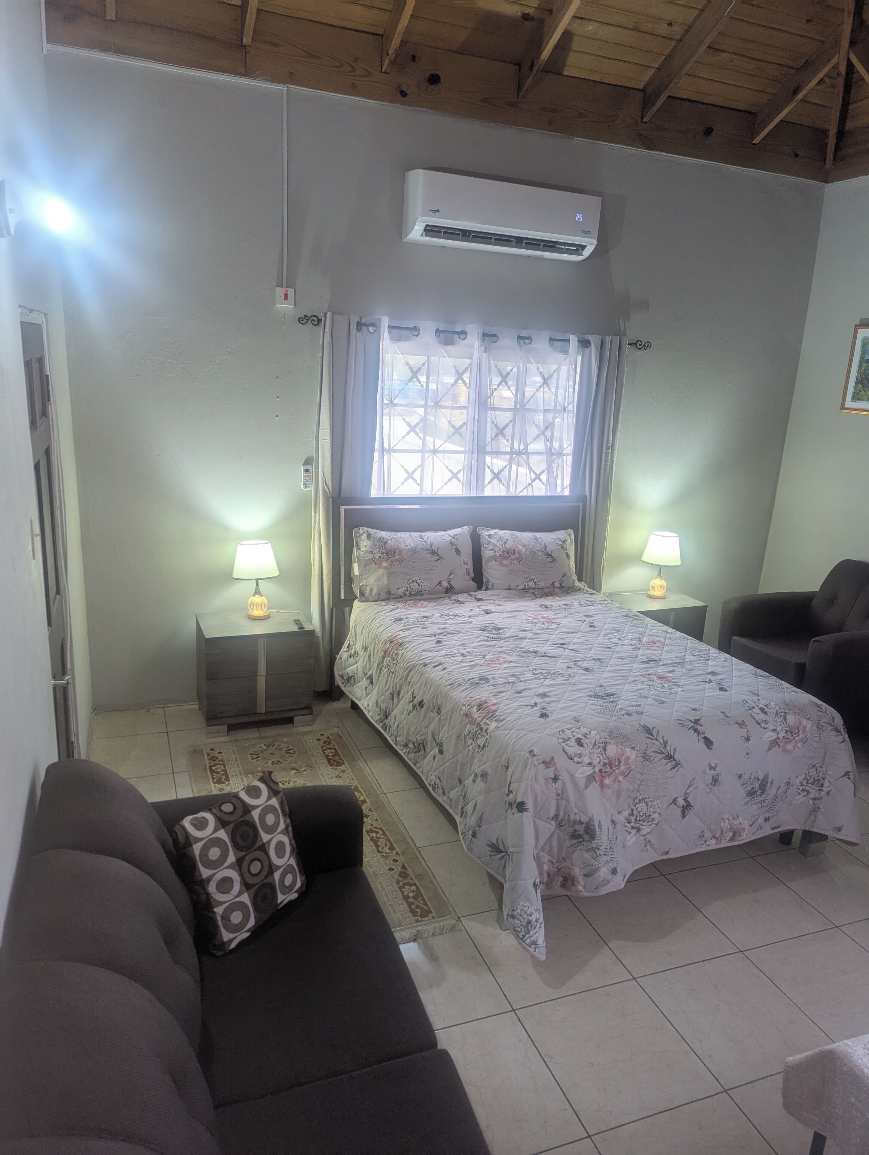 Une chambre à coucher avec un lit, deux tables de chevet avec des lampes, un plafond en bois et un appareil de climatisation.