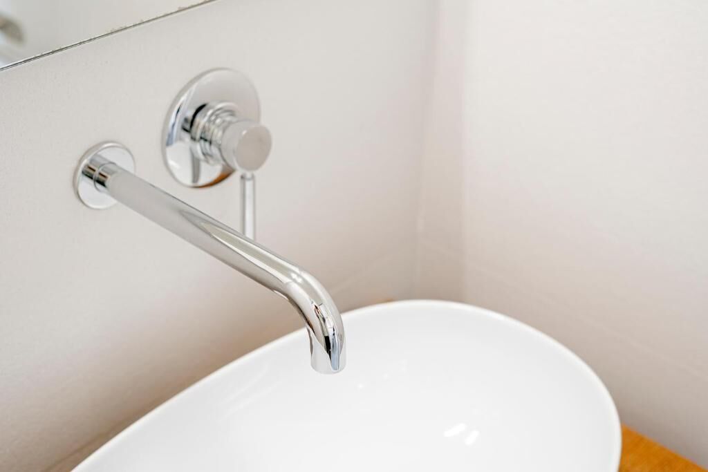 Een wastafel met een chromen kraan en een ronde, aan de muur bevestigde hendel.