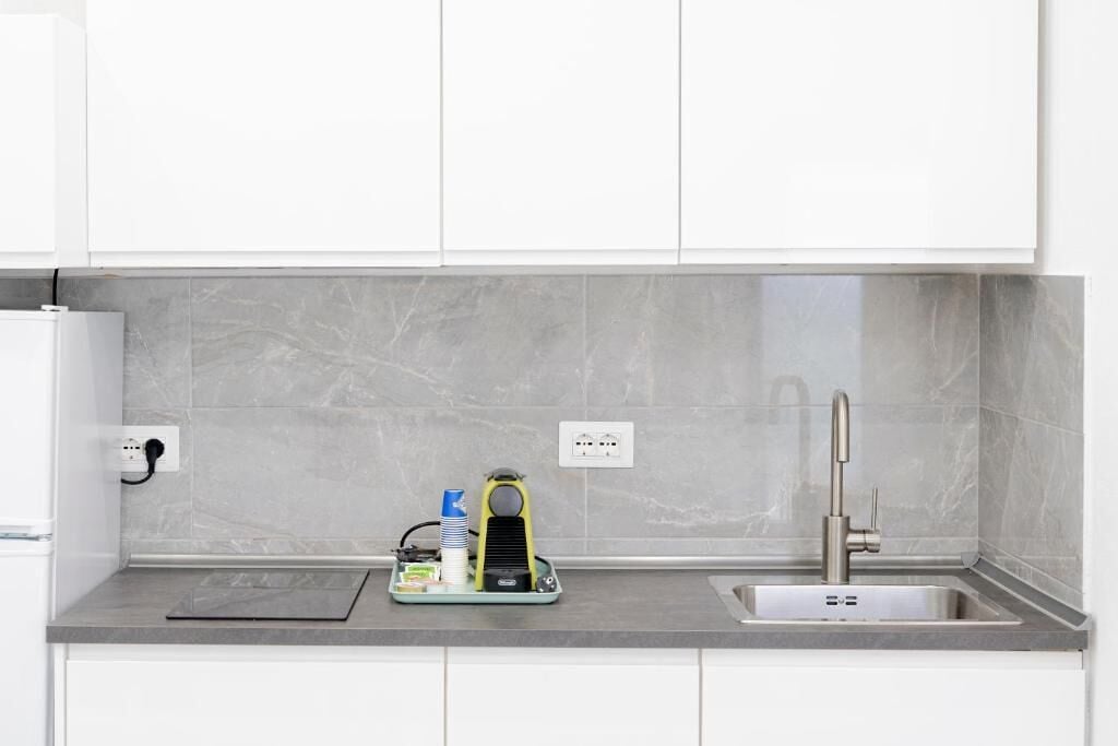 Una cocina moderna con protector contra salpicaduras de mármol gris, un lavamanos de acero inoxidable y un horno empotrado.
