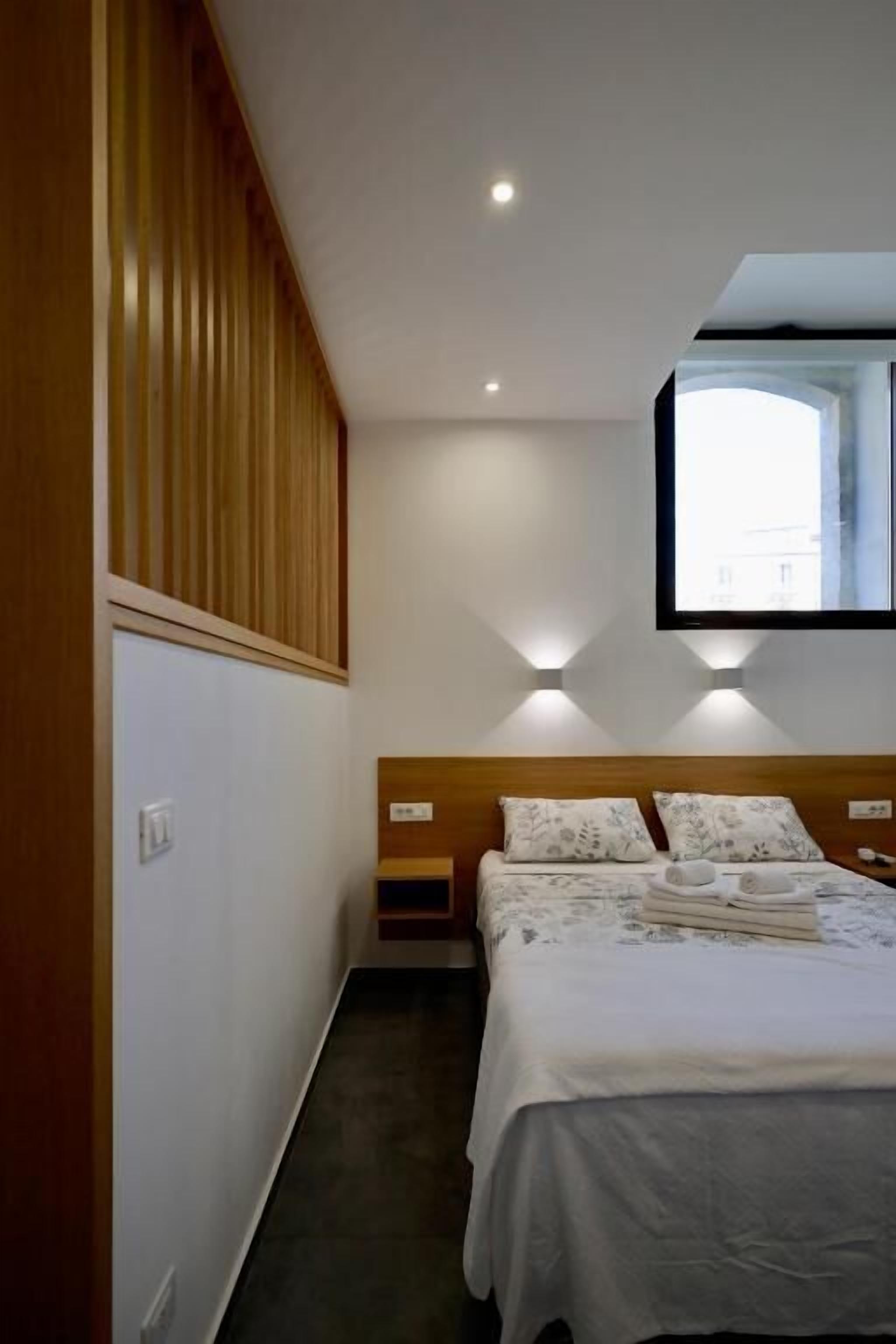 A bedroom with a bed, wooden paneling, a wall-mounted TV, and recessed lighting.