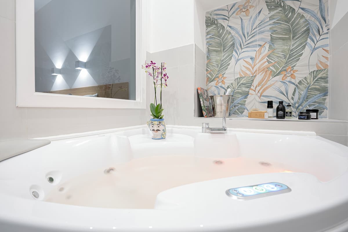 Een moderne badkamer met een groot bad, een decoratieve vaas met bloemen en een muur met een tropisch bladmotief.