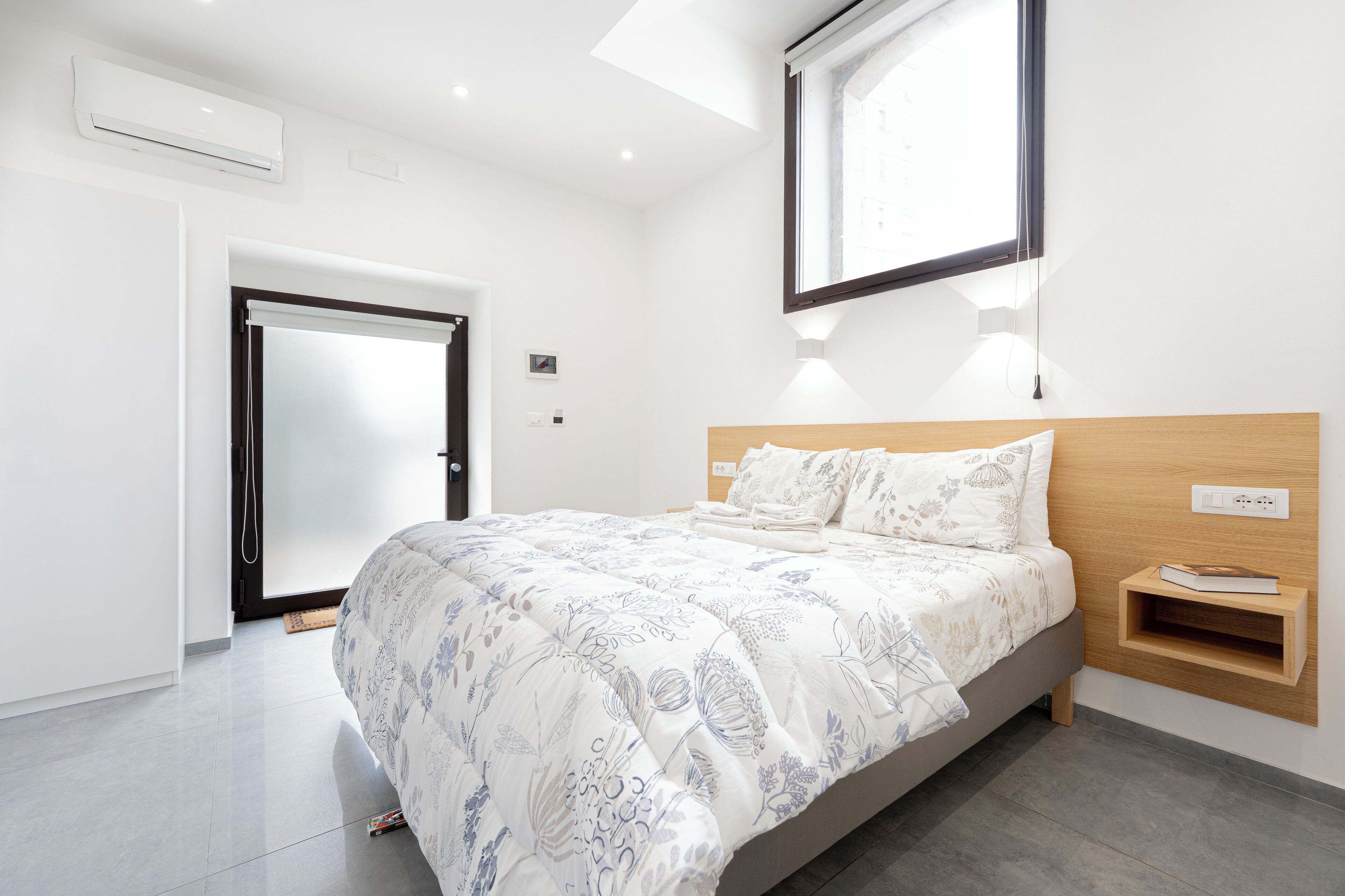Une chambre moderne avec un grand lit, une tête de lit en bois, une table de chevet et une étagère intégrée.