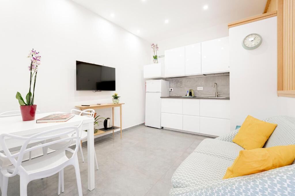 A modern kitchen with white cabinets, a built-in oven, and a microwave. There is a dining table with chairs and a small plant on it.