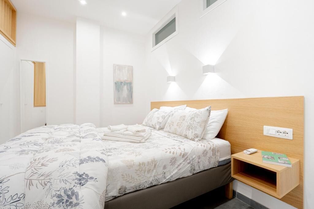 Une chambre bien rangée, avec un lit, une table de chevet et une étagère fixée au mur.