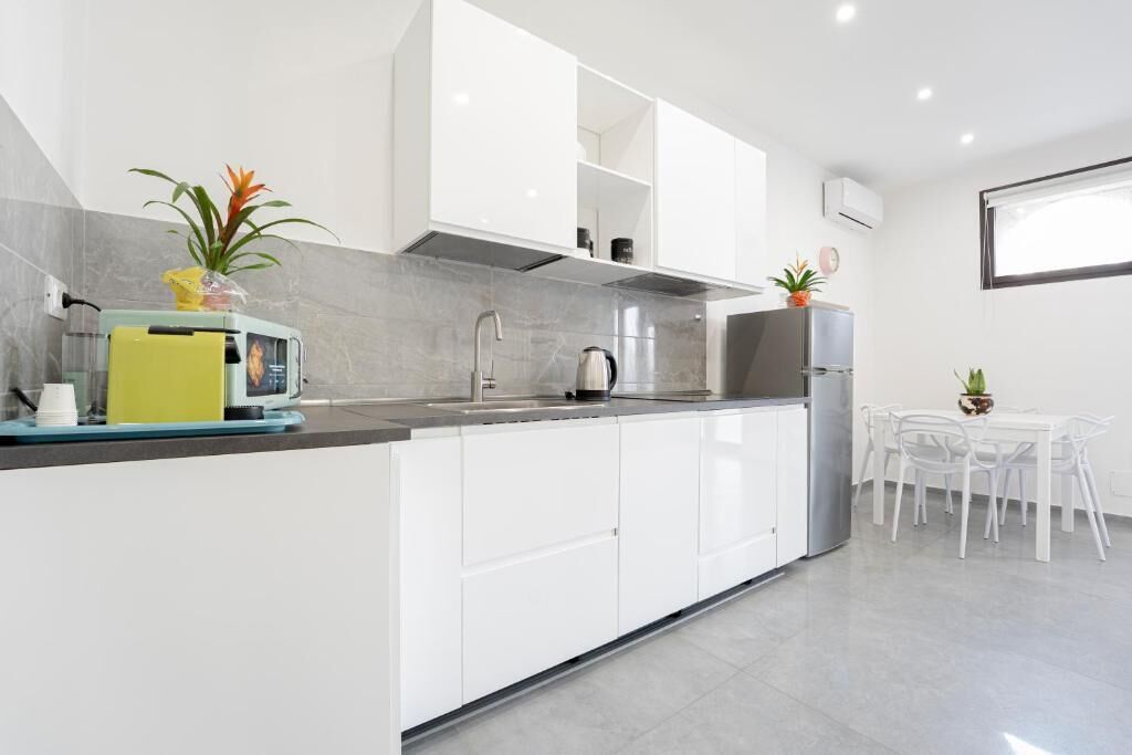 A modern kitchen with white cabinets, a grey countertop, and a dining area with a white table and chairs.