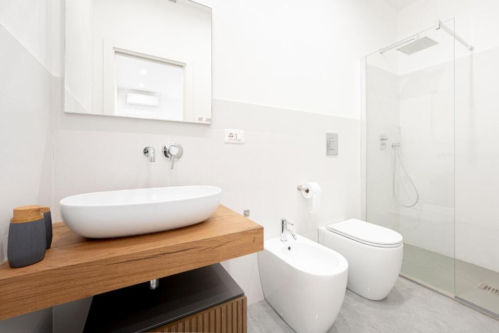 Een moderne badkamer met een groot wit wastafel, een houten wastafelmeubel, een wit toilet en een douche met glazen wanden.