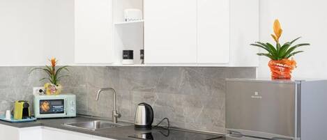 A modern kitchen with white cabinets, a stainless steel refrigerator, a kettle, a microwave, and a sink.