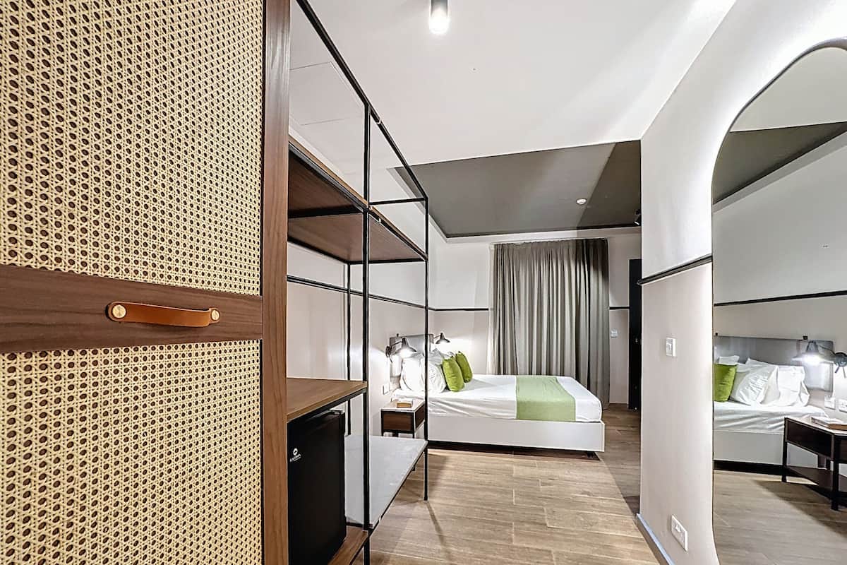 Een moderne hotelkamer met een houten garderobe, een bed met groene kussens en een apart slaapgedeelte.