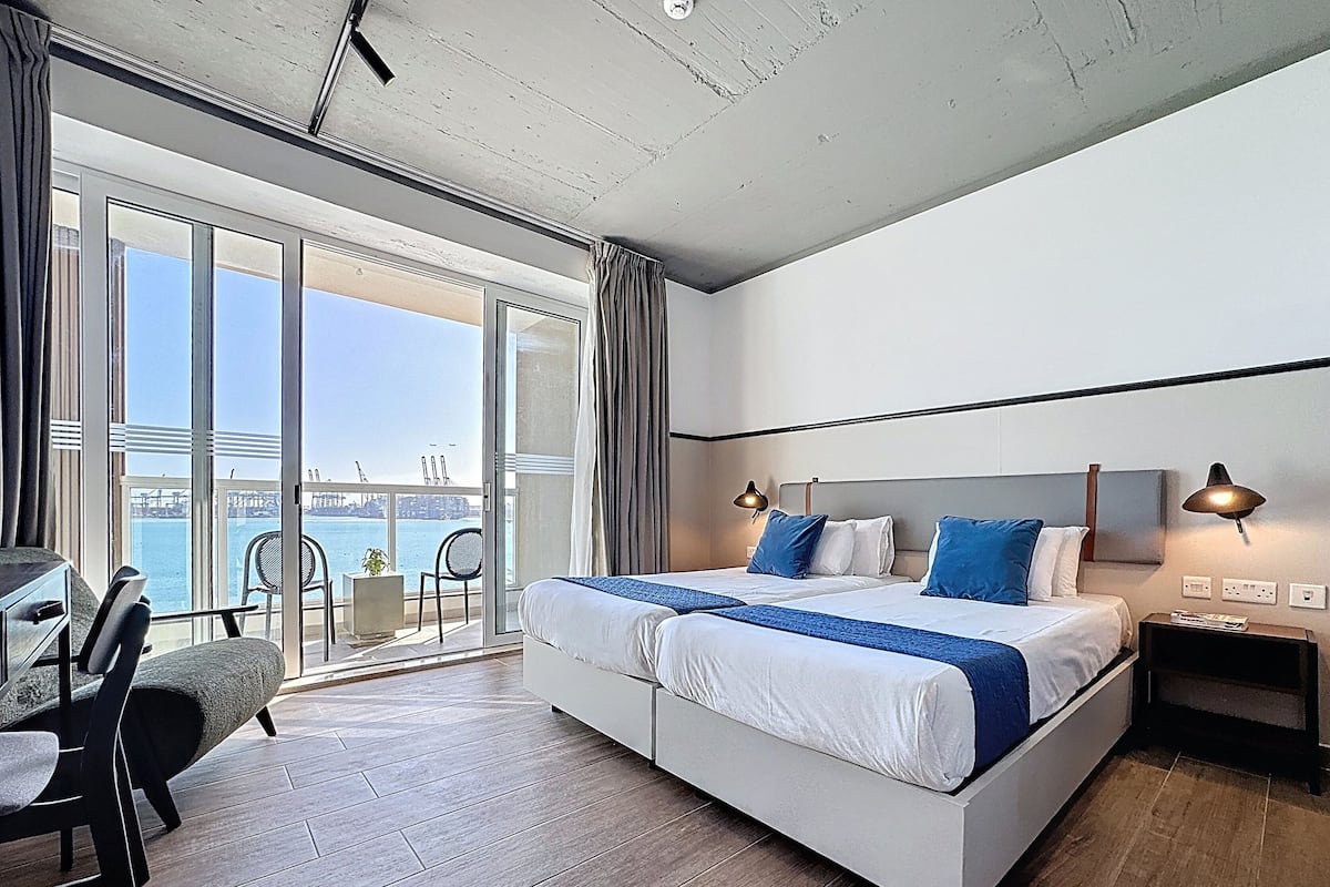 Een moderne hotelkamer met een groot bed, een bureau en een balkon met uitzicht op zee.