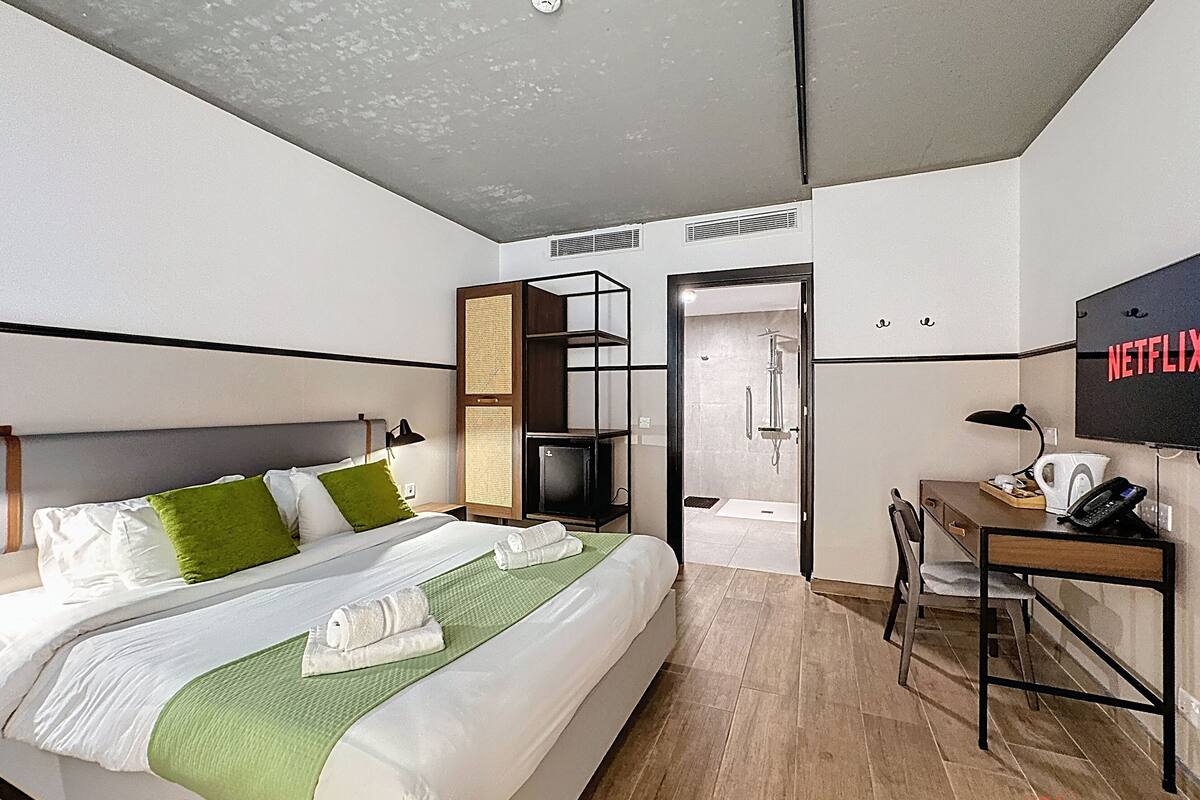 Een moderne hotelkamer met een bed, een bureau, een douche en een televisie met de tekst 'NETFLIX'.