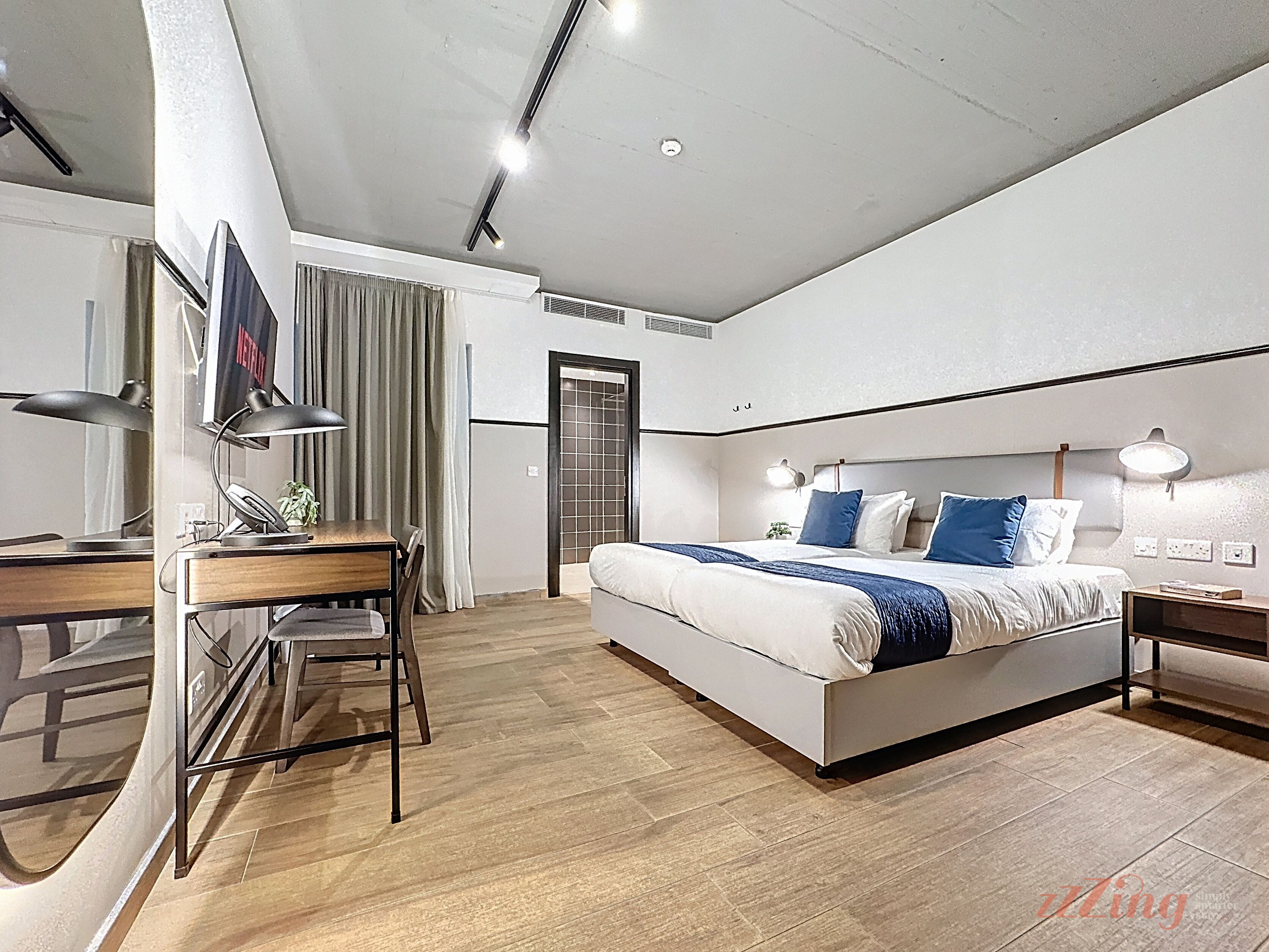 A modern hotel room with a bed, desk, and chair, a TV, and a door.