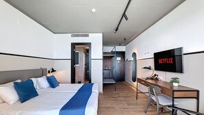 A hotel room with a bed, desk, chair, TV, and a bathroom visible through an open door.