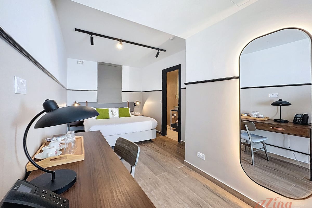 Een kleine hotelkamer met een bed, bureau met telefoon, spiegel en een kitchenette.