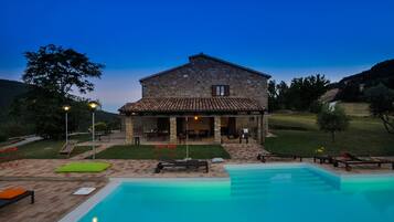 A stone house with a tiled roof, a swimming pool, and outdoor seating.