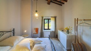 Ein Schlafzimmer mit Bett, Nachttisch, Fenster und einer Pendelleuchte.