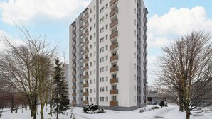 Un immeuble résidentiel de grande hauteur, doté de nombreux balcons, entouré d’arbres sans feuilles et d’un sol recouvert de neige.