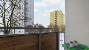 Un balcon doté d’une séparation en bois, une table verte agrémentée de deux plantes en pot et une vue sur de hauts immeubles.