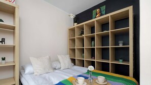 Une chambre à coucher bien rangée, avec un lit, une table de chevet sur laquelle se trouvent des tasses et un vase, et une grande bibliothèque.