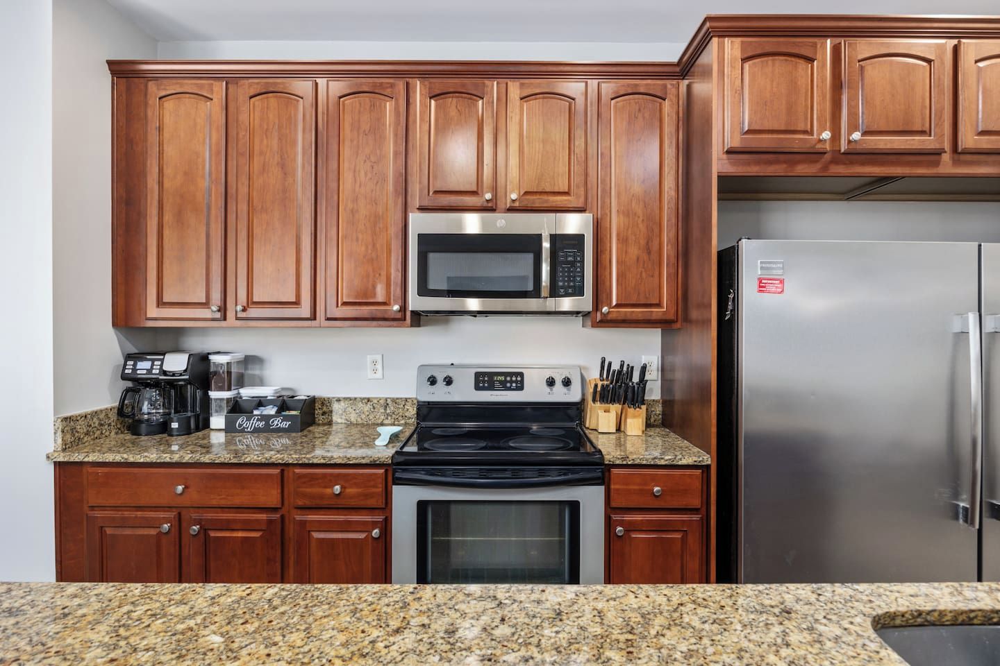 A kitchen with wooden cabinets, a microwave, a stove, a refrigerator, and a coffee maker on the counter.