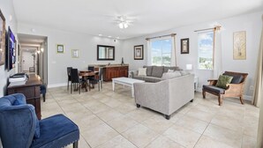 Un salón espacioso con un sofá gris, un sillón azul, un comedor con una mesa redonda y una cocina al fondo.