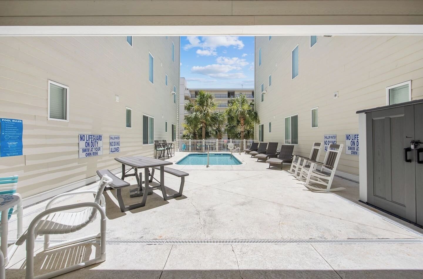 A pool area with a table and chairs, a lifeguard station, and signs indicating no lifeguard on duty.