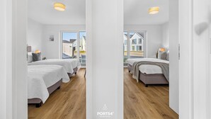 Una habitación de hotel moderna con dos camas, suelo de madera y grandes ventanales con vistas a la calle.