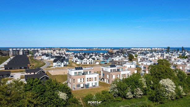 Una zona residencial costera con casas modernas, cielo despejado y vista al mar.