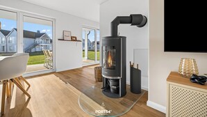 Una sala de estar moderna con una mesa de vidrio, un estufa de leña negra y un televisor instalado en la pared.