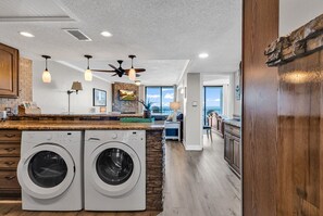 A modern kitchen with built-in washers, a stone backsplash, and a large island with pendant lighting. - Windy Hill Beach-Sleeps 7-3bed/2bath-Oceanfront-Pool-WIFI-TV-16 Foot Balcony (North Myrtle Beach)