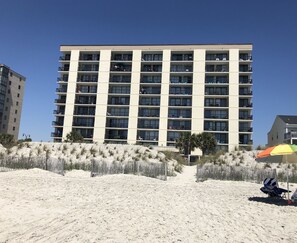A multi-story hotel with balconies, located on a sandy beach with a wooden fence and palm trees. - Windy Hill Beach-Sleeps 7-3bed/2bath-Oceanfront-Pool-WIFI-TV-16 Foot Balcony (North Myrtle Beach)
