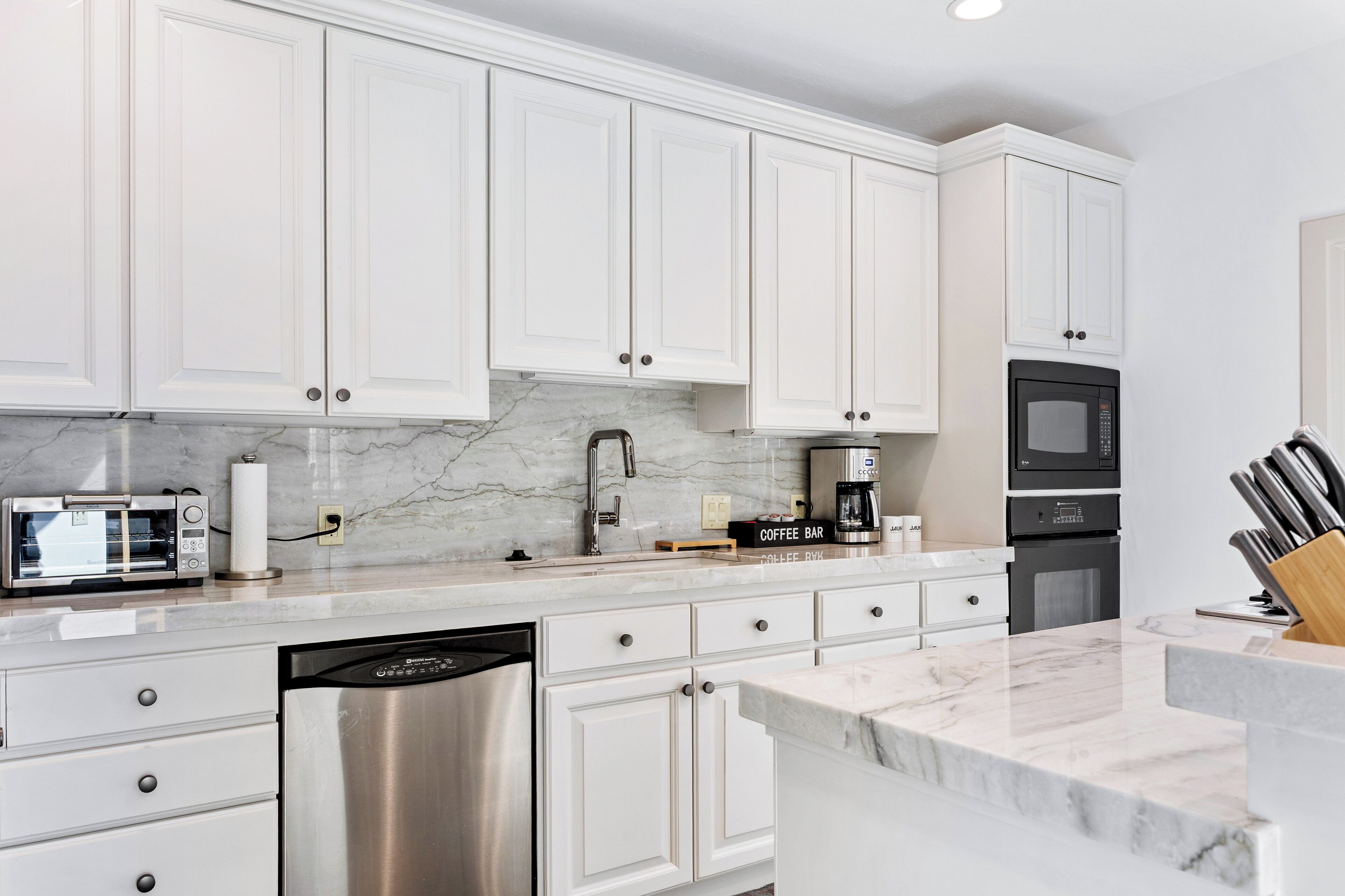 A modern kitchen with white cabinets, a built-in microwave, a coffee maker, and a dishwasher.