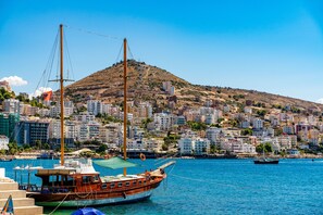 Un paysage urbain côtier avec une colline imposante, un bateau amarré et un ciel bleu dégagé.