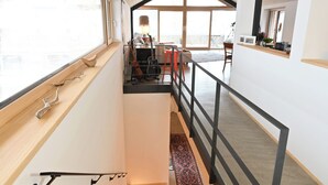 Un intérieur moderne avec un escalier en bois, un bureau avec un ordinateur et une vue dégagée grâce à de grandes fenêtres.