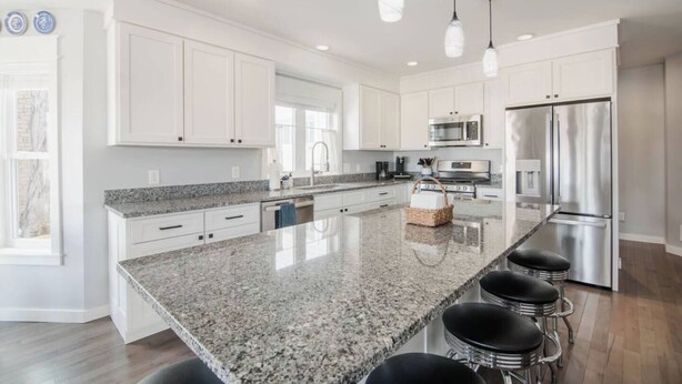 A modern kitchen with white cabinets, granite countertops, stainless steel appliances, and pendant lighting. - High Tide: Harbor View: Walk2town/Beach: sleeps 12 (Boyne City)