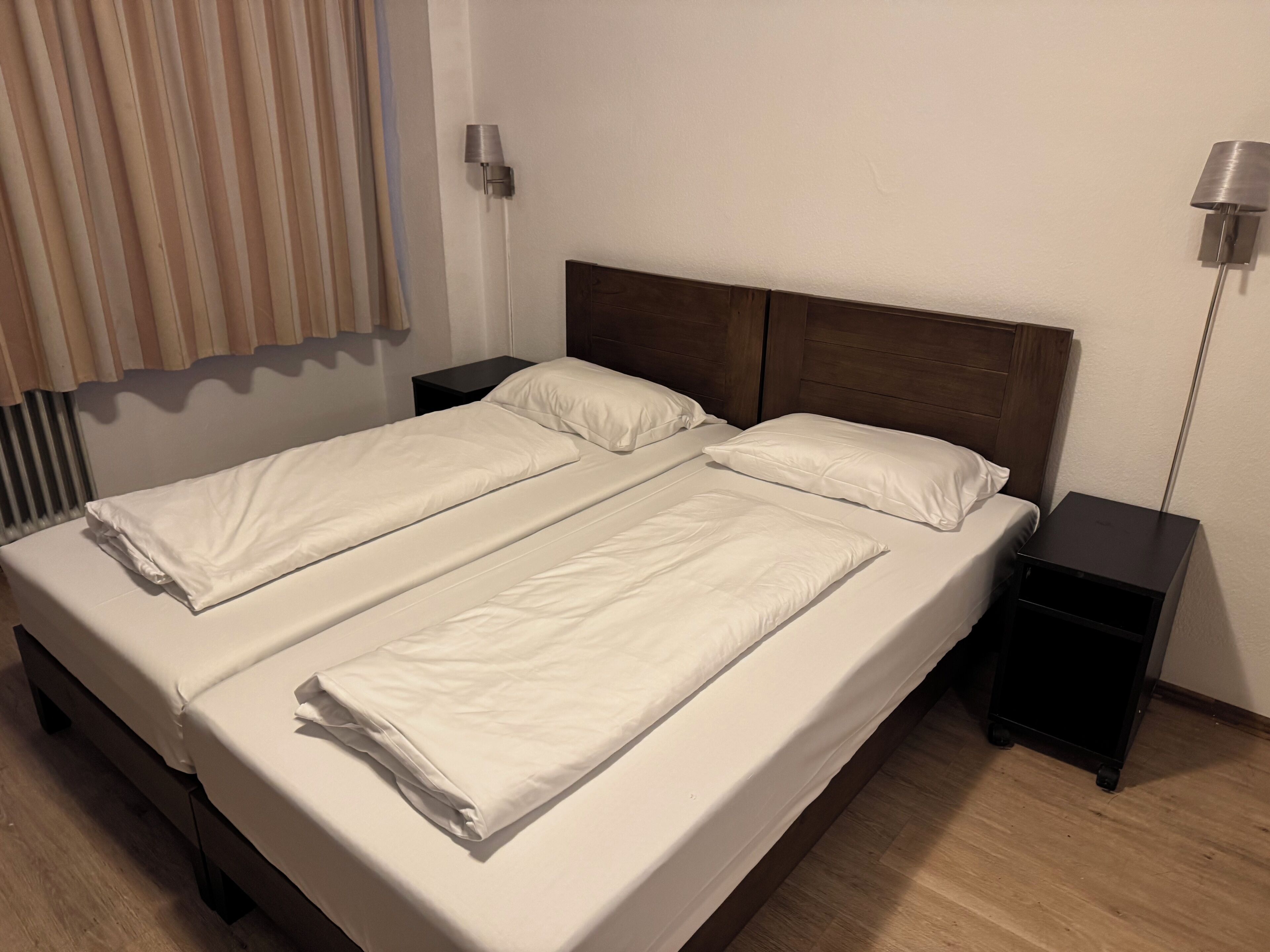 A double bed with white linens, two bedside tables, and a wall-mounted lamp.
