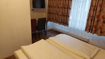 Camera d'albergo con un letto, una scrivania, una sedia, una televisione a muro e una finestra con tende.