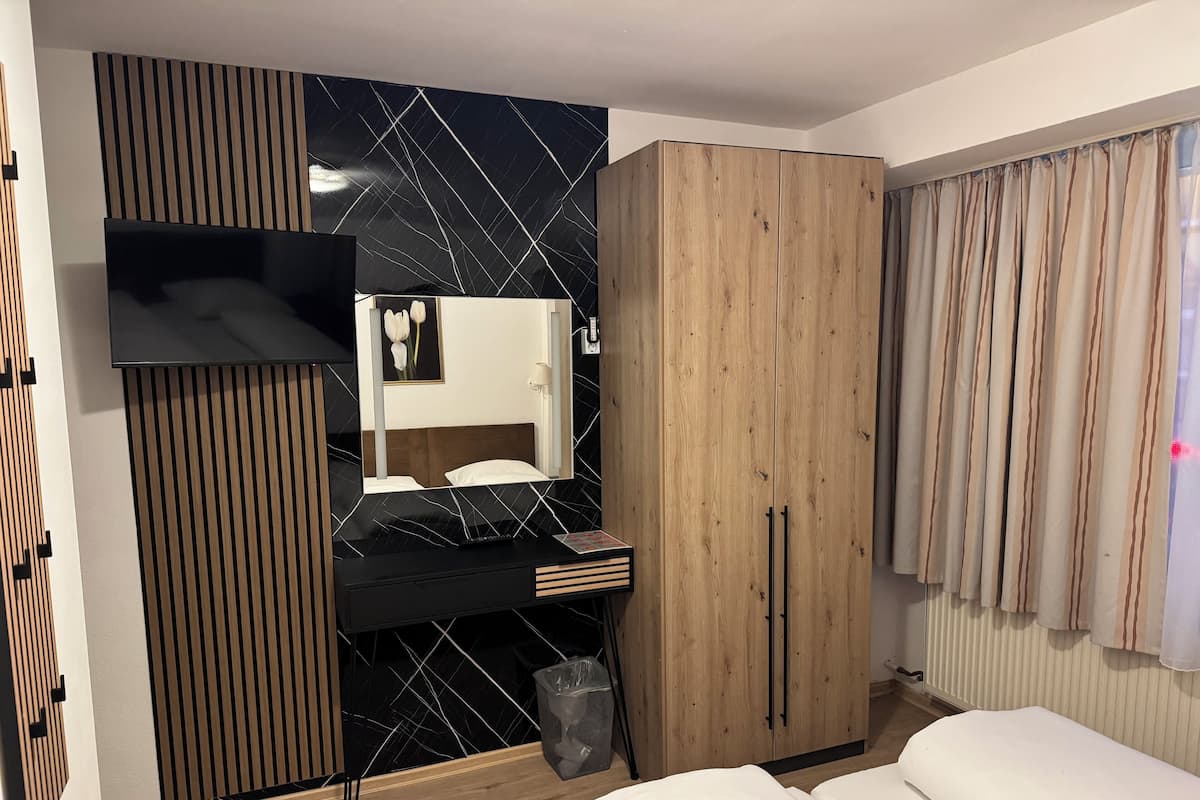 A modern bedroom with a black and white patterned wall, a wooden wardrobe, a bedside table, and a white bed.