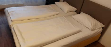 A double bed with white bedding and a wooden headboard in a room with wooden flooring.