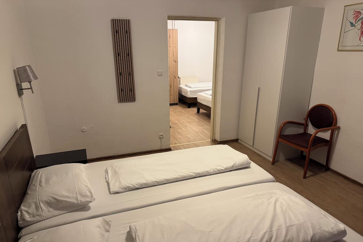 A bedroom with two single beds, a wooden chair, a bedside lamp, and a wooden panel on the wall.